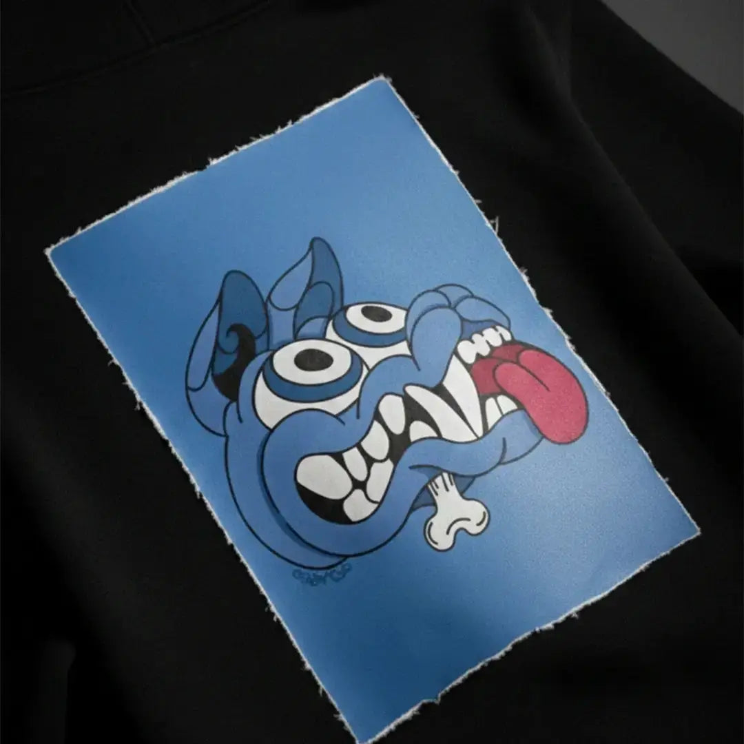 Patch magnetica Cryptic Mad Dog blu su felpa Cryptic nera, design cartoon con espressione folle, toppa personalizzabile e removibile.