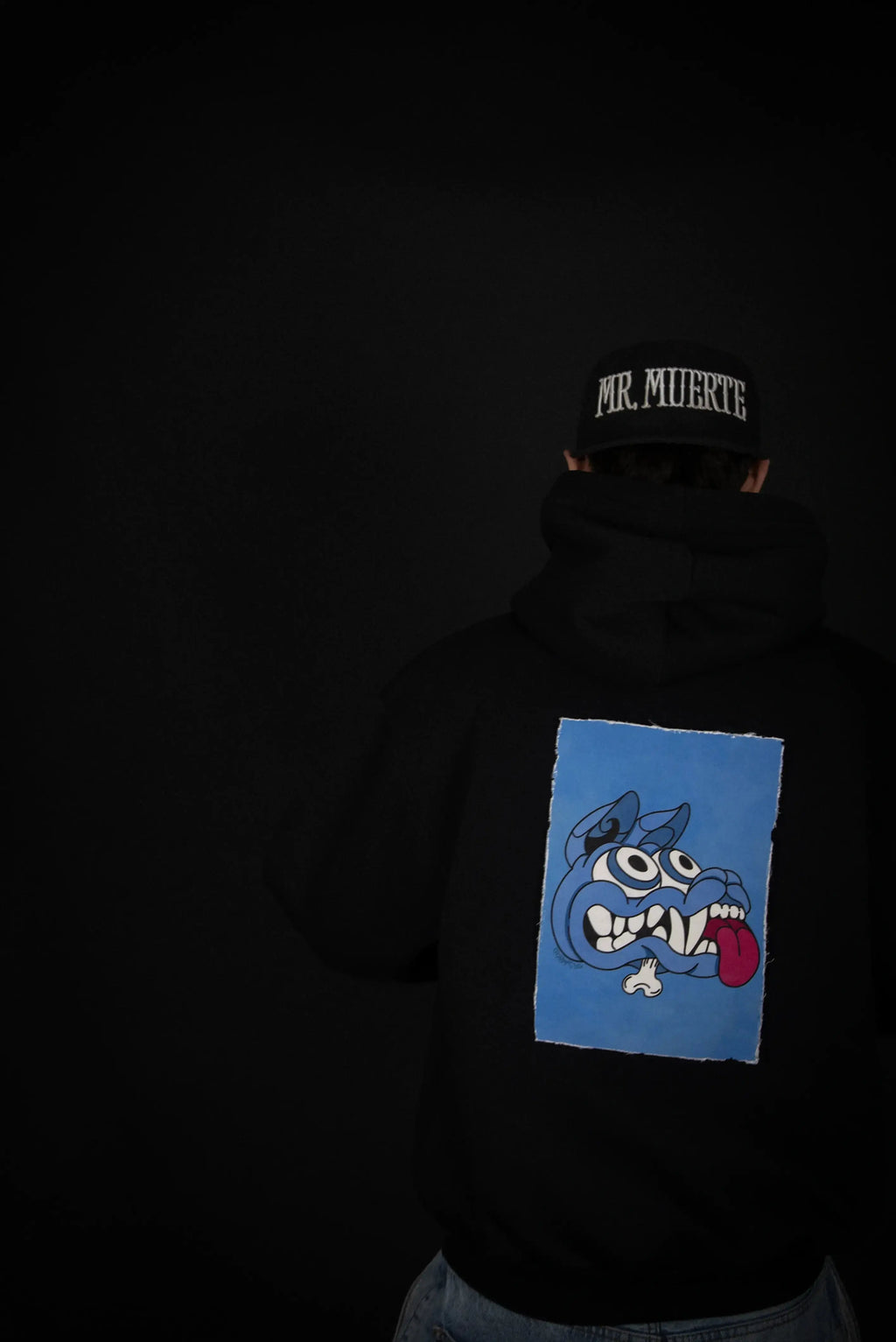 Hoodie Cryptic con toppa magnetica blu Mad Dog sul retro, indossata da modello con cappellino, perfetta per look urban e versatili.