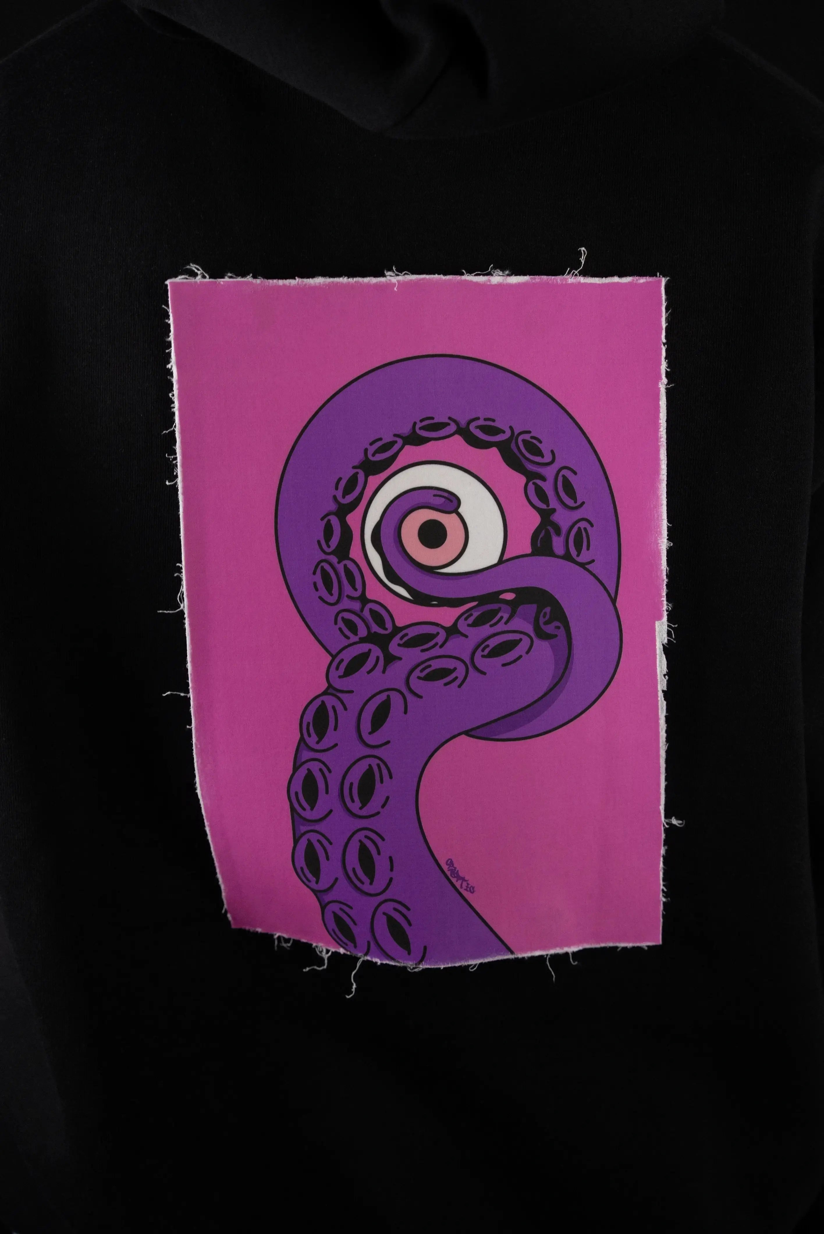 Patch intercambiabile Cryptic EnKrak con design artistico di tentacolo viola, bordo sfrangiato su felpa Cryptic nera, ideale per look personalizzati.